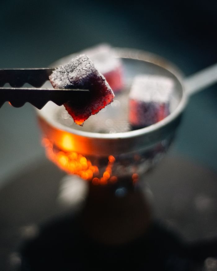 Close-up of glowing hookah charcoal with tongs in dim lighting, ideal for nightlife concepts.